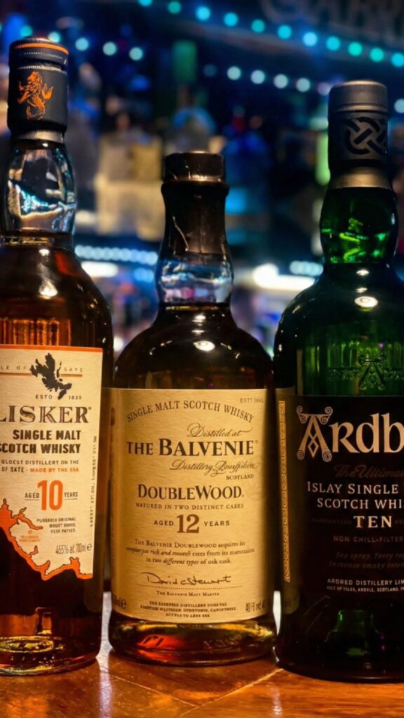 Talisker 10, The Balvenie DoubleWood 12 y Ardbeg 10, en la barra de un bar con ambiente acogedor.
